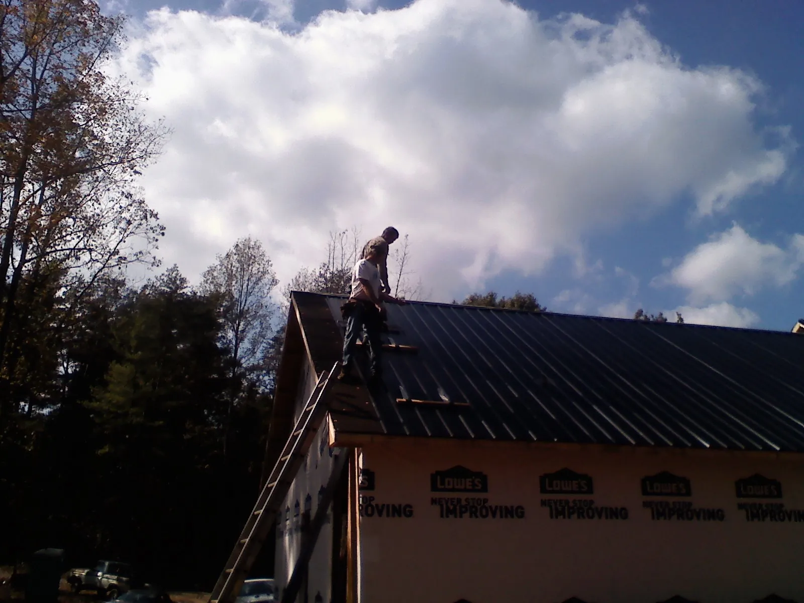 Roofer fastening dark metal panels high against a cloudy sky, from a Roof Inspection job in Washtucna