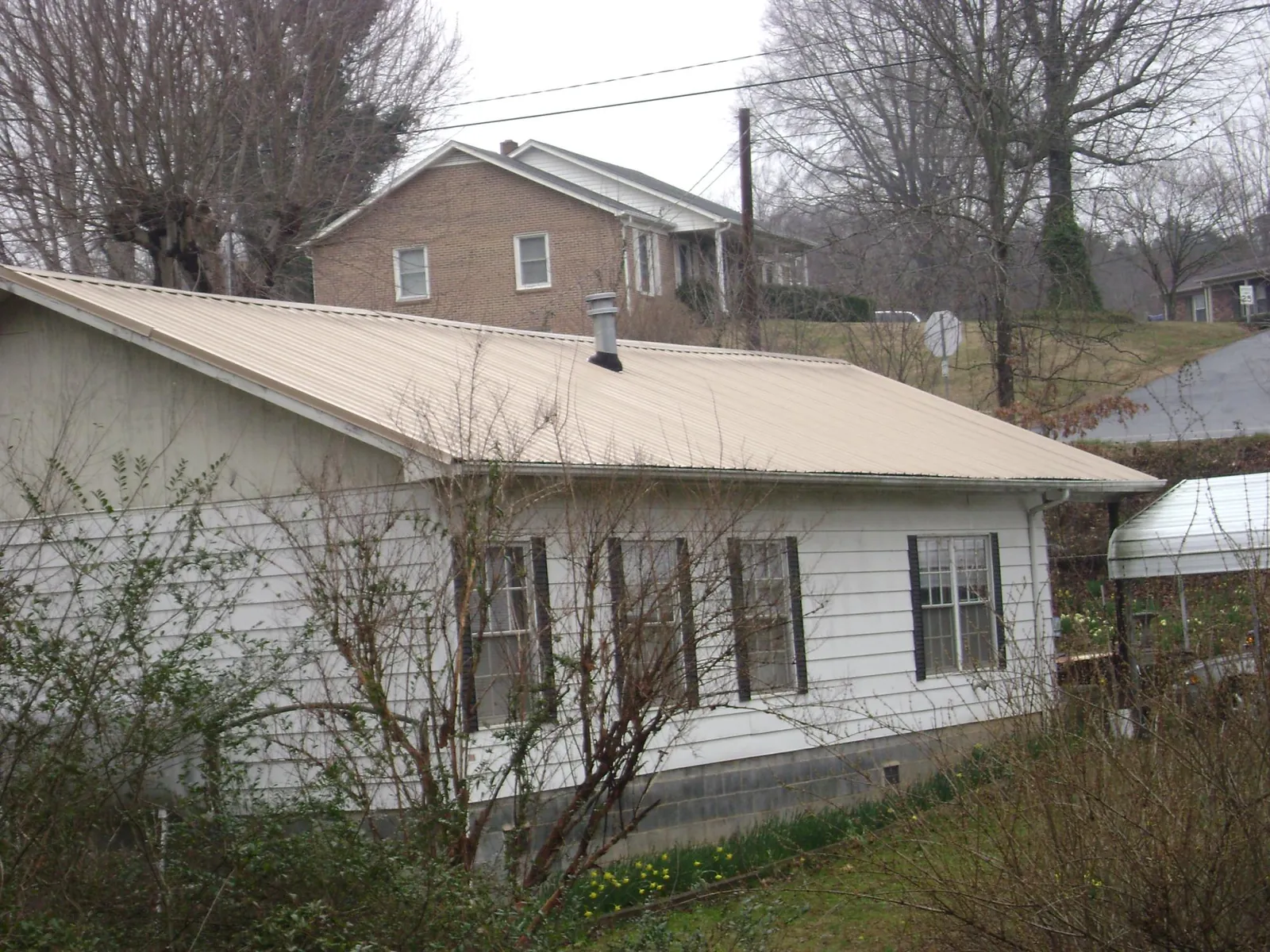 Tan metal roof on a white sided house set into a hillside — Commercial Roofing by Roofing Brothers in Washtucna